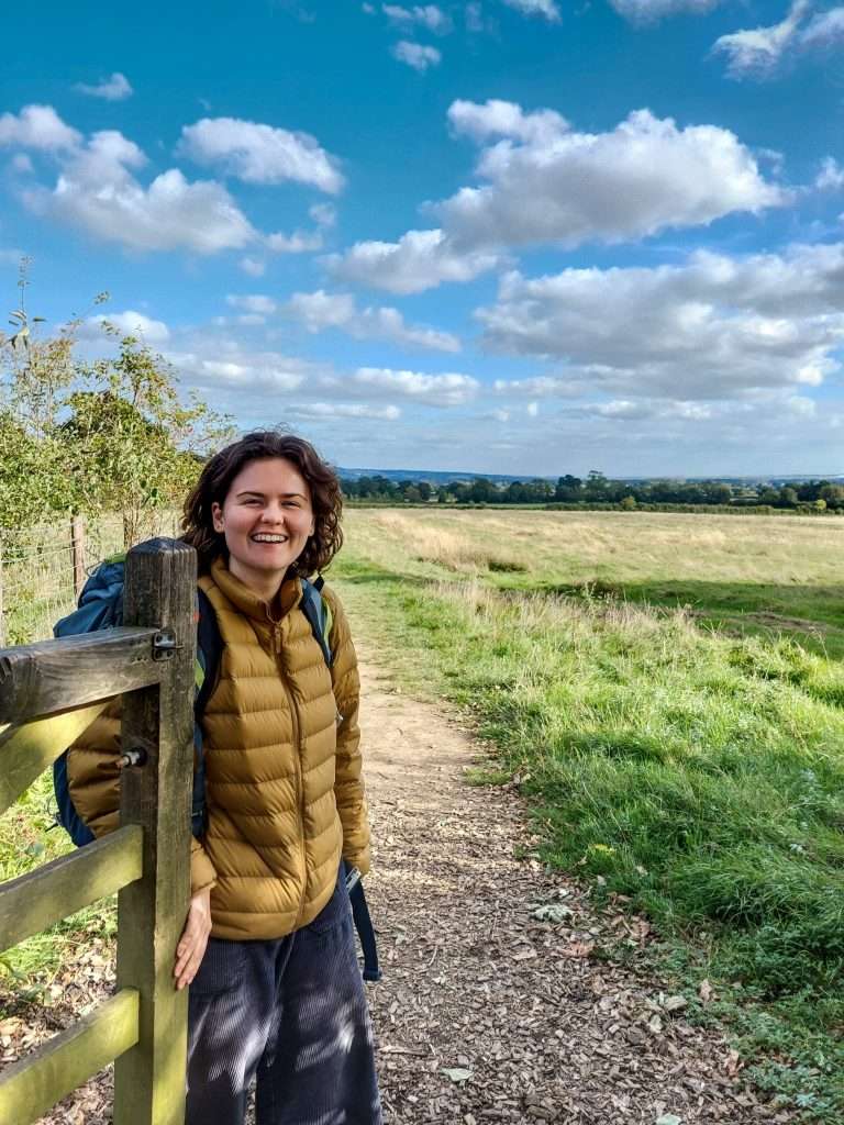 Image of Lauren, the life coach, in a field on a summer's day holding a gate open for a friend